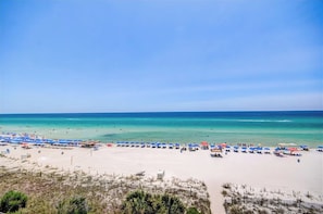 Ein Strand mit vielen Sonnenschirmen und Liegestühlen, feinem Sand und klarem, blauem Wasser.