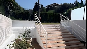Una serie di gradini esterni che portano a un terrazzo con piante in vaso e una ringhiera bianca.