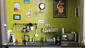 Cozinha com parede verde, pia, micro-ondas e frigorífico. Inclui utensílios de cozinha diversos e uma máquina de café.