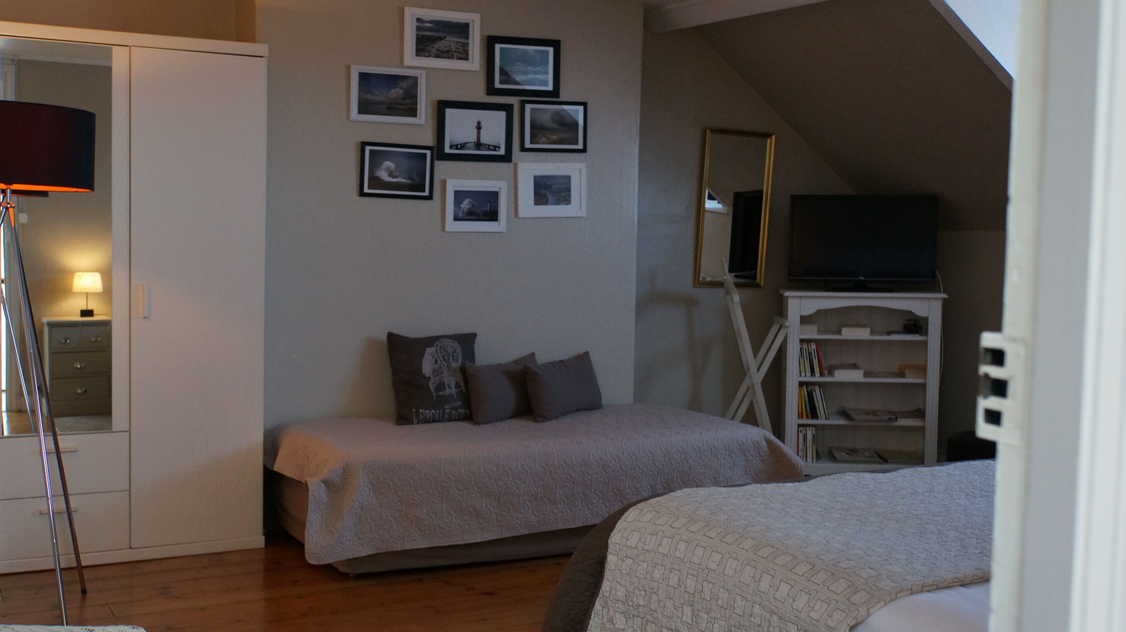A bedroom with a bed, a TV, a bookshelf, and a wall with framed pictures.