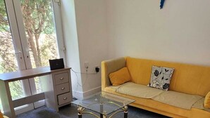 En stue med en gul sofa, et glasbord og et træskrivebord.