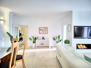 Ein modernes Wohnzimmer mit einem weißen Sofa, einem Glastisch und einem wandmontierten Flachbildfernseher.