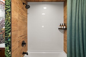 A shower area with a wooden wall, a white tiled shower enclosure, a black showerhead, and a shelf with bottles.