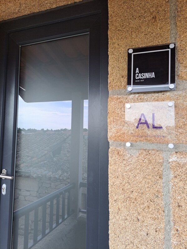 Una puerta con vista a un edificio de piedra y un letrero que dice 'A CASINHA' y 'AL'.
