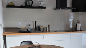 A modern kitchen with a round wooden table, two black chairs, and a coffee maker.