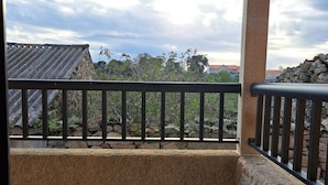 A balcony with a stone wall, a metal railing, and a view of a traditional building with a tiled roof.