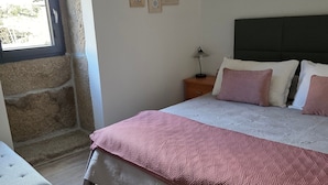 A bedroom with a bed, a nightstand, a lamp, a window, and a wall with framed pictures.