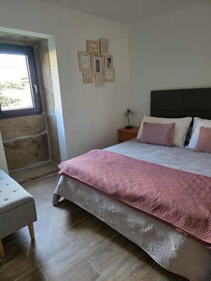 Un dormitorio con una cama, una mesita de noche, una lámpara, una ventana y una pared decorada con marcos.