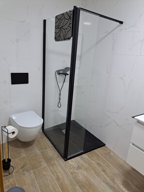 Un baño con ducha envuelta en vidrio, un inodoro y un lavabo.