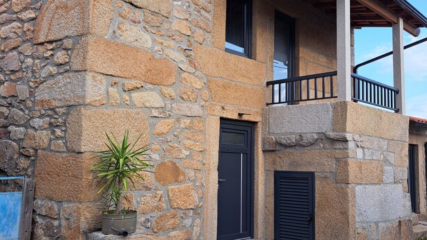 A stone building with a balcony, a potted plant, and a mailbox.