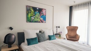 Una habitación de hotel moderna con una cama grande, un escritorio, una silla y un cuadro abstracto y colorido en la pared.
