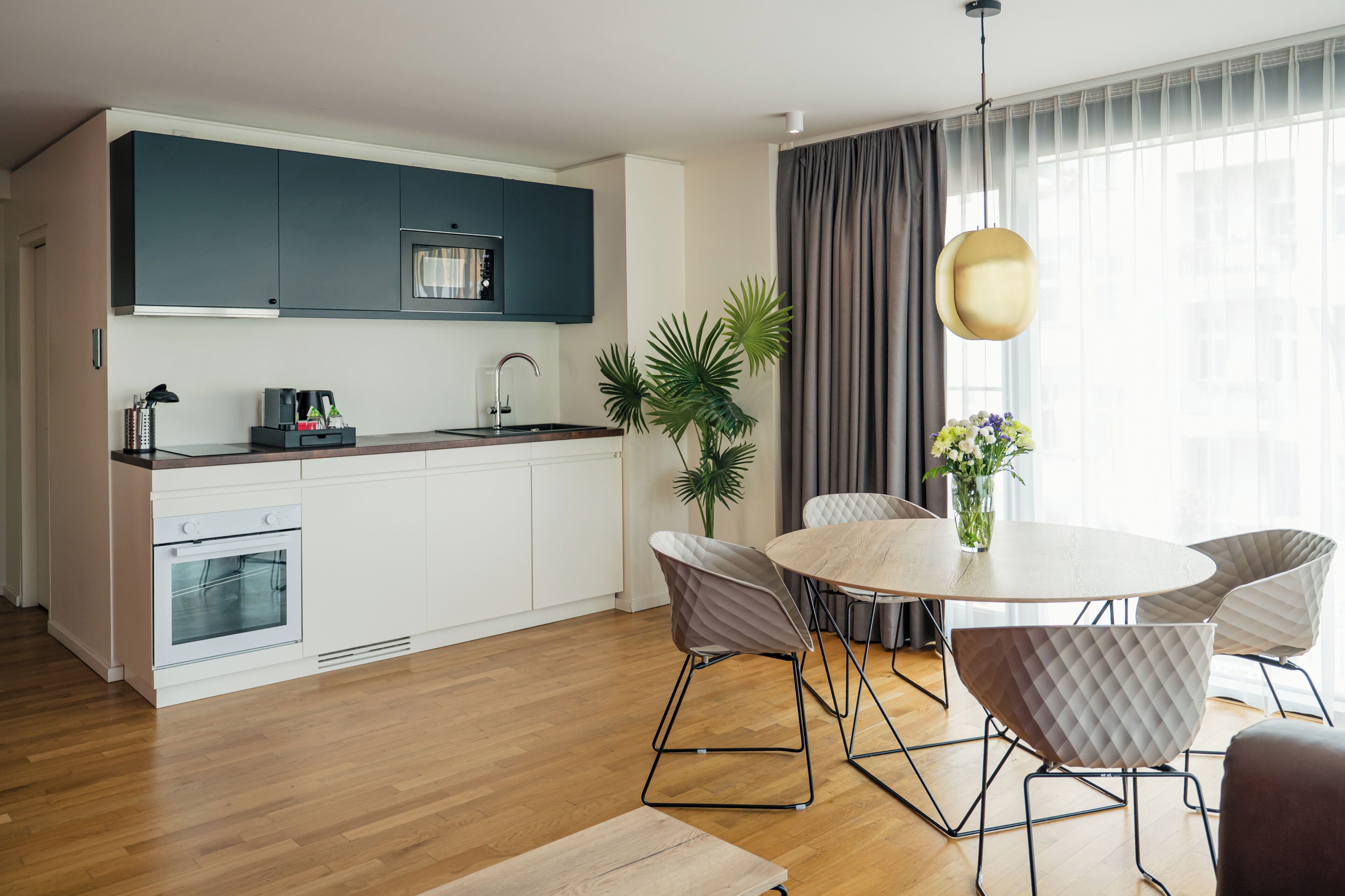 A modern kitchen with white cabinets, a built-in oven, and a microwave. There is a dining area with a round table and four chairs.