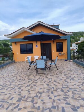 A house with a tiled patio, a table with chairs, and a large umbrella. - Family Residential (San Agustín de las Juntas)