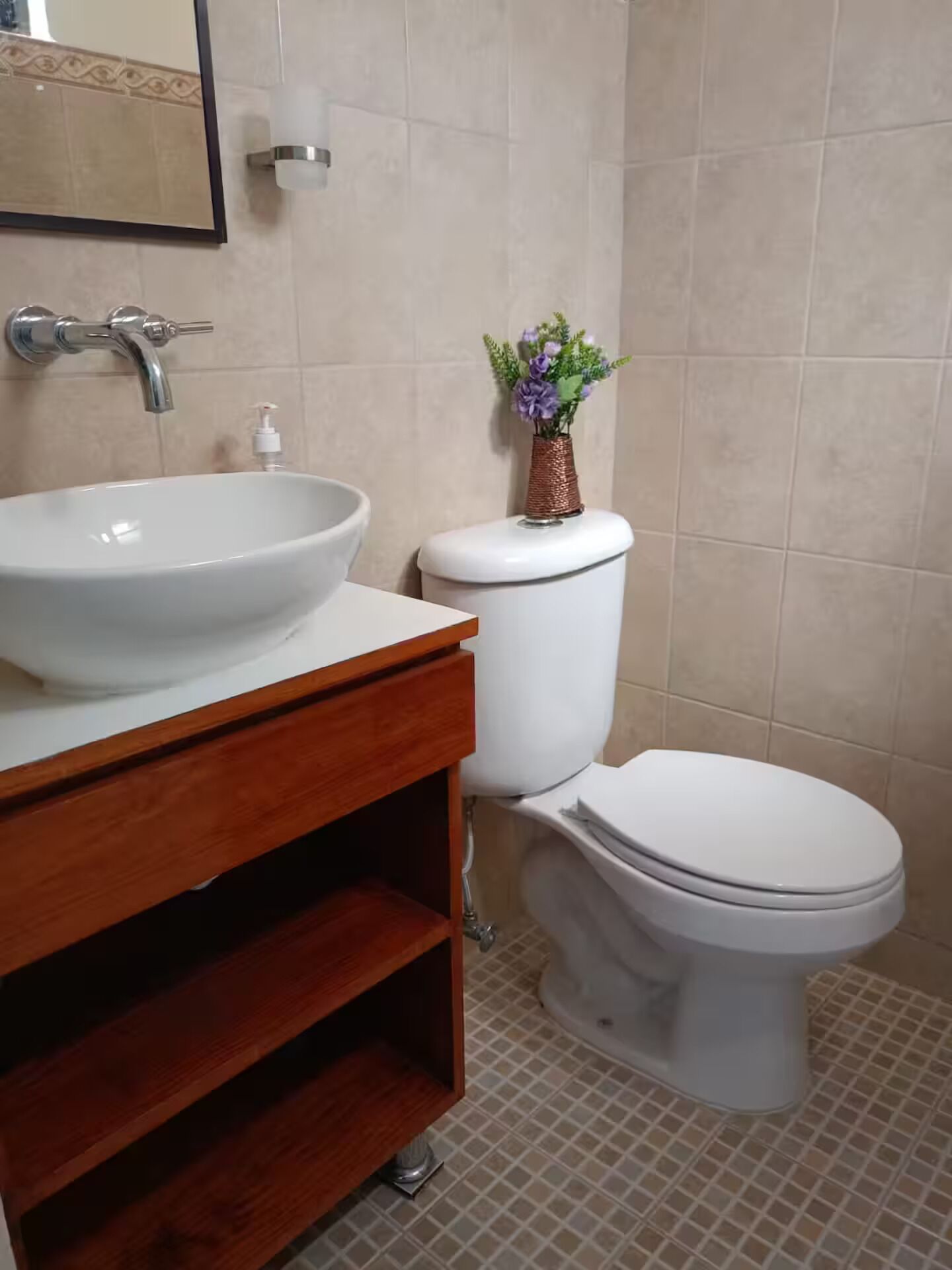Une salle de bain avec un lavabo blanc, un meuble-lavabo en bois, des toilettes et un petit vase avec des fleurs.