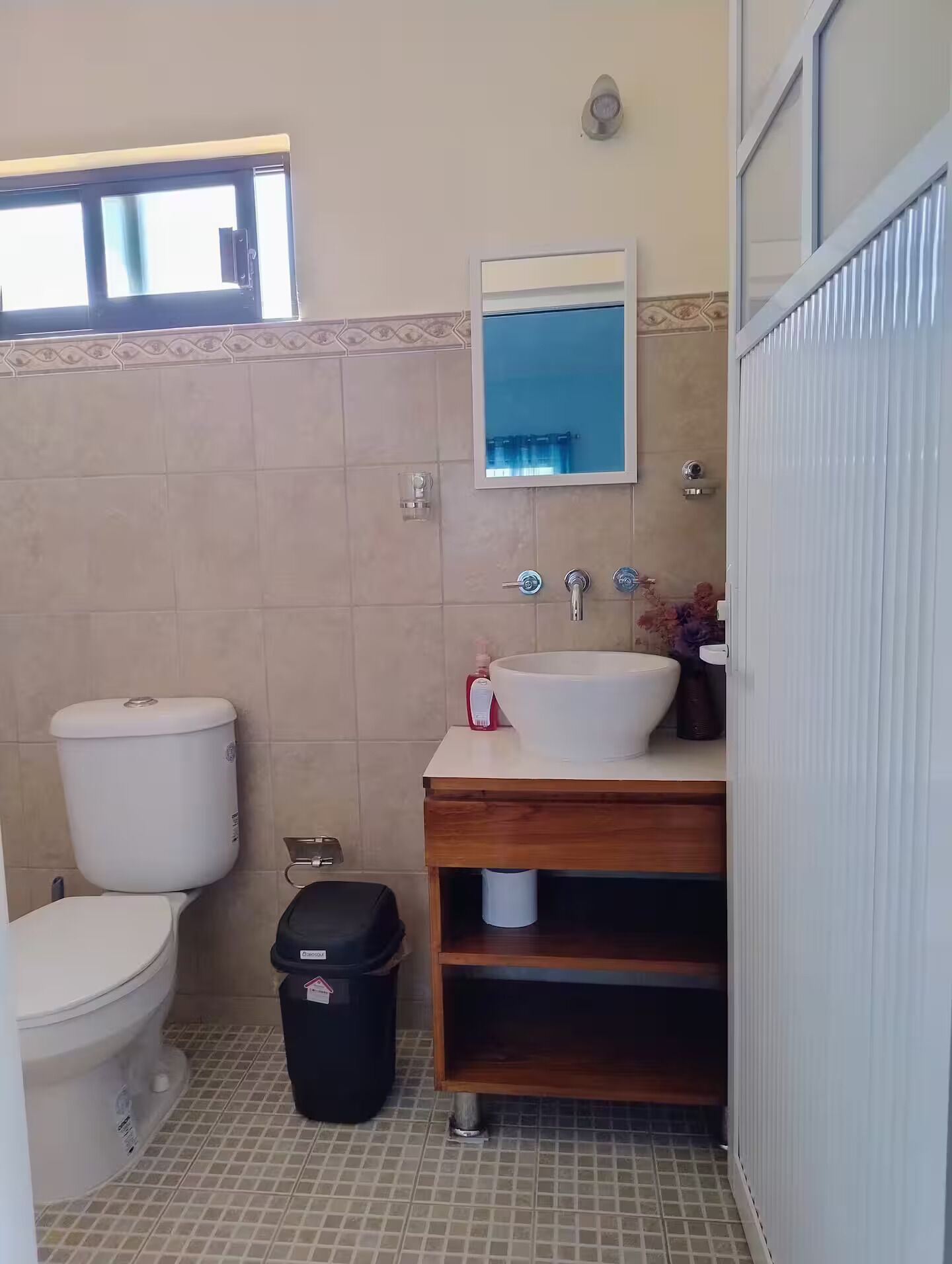 A bathroom with a toilet, sink, mirror, and tiled floor.