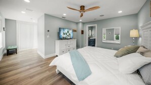 A bedroom with a bed, a dresser, a television, a ceiling fan, and a window.
