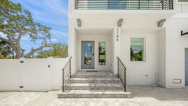 A modern two-story building with a white exterior, a gated entrance, and a staircase leading to the main door.