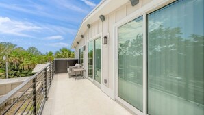 A modern building with large glass windows, a balcony with outdoor furniture, and a view of greenery.