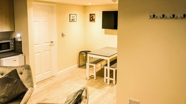 A compact living space with a kitchenette, a dining area, and a TV mounted on the wall. - Apartment Sleeps 4 With Parking (Blakeney)