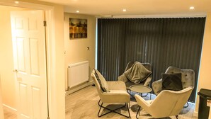 A room with a door, a radiator, two armchairs, a small round table, and a dark curtain. - Apartment Sleeps 4 With Parking (Blakeney)