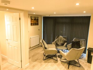 Ein Zimmer mit Tür, Heizkörper, zwei Sesseln, einem kleinen runden Tisch und einem dunklen Vorhang.