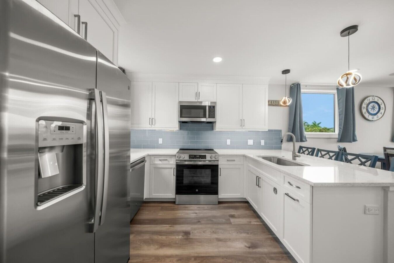 A modern kitchen with stainless steel appliances, white cabinetry, and a wooden floor.