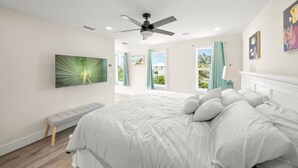 A bedroom with a bed, a ceiling fan, a bench, and a window with curtains.