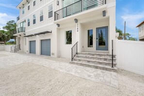 Un edificio moderno de varios pisos con techo plano, un balcón en el segundo nivel y una puerta de garaje.