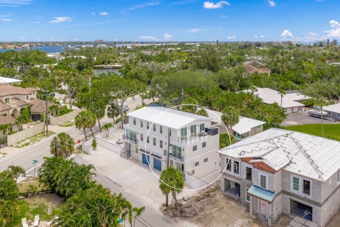 A residential area with a modern two-story house featuring a balcony, a driveway, and a view of a body of water.