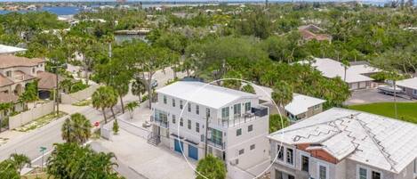 A residential area with a modern two-story house featuring a balcony, a driveway, and a view of a body of water.