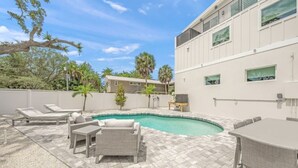 A pool area with lounge chairs, a table, and a building with large windows.