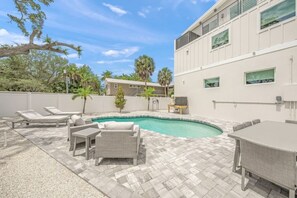 A pool area with lounge chairs, a table, and a building with large windows.