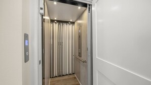 An elevator interior with a control panel, a vertical striped wall, and a wooden floor.