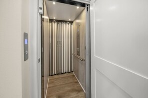 An elevator interior with a control panel, a vertical striped wall, and a wooden floor.