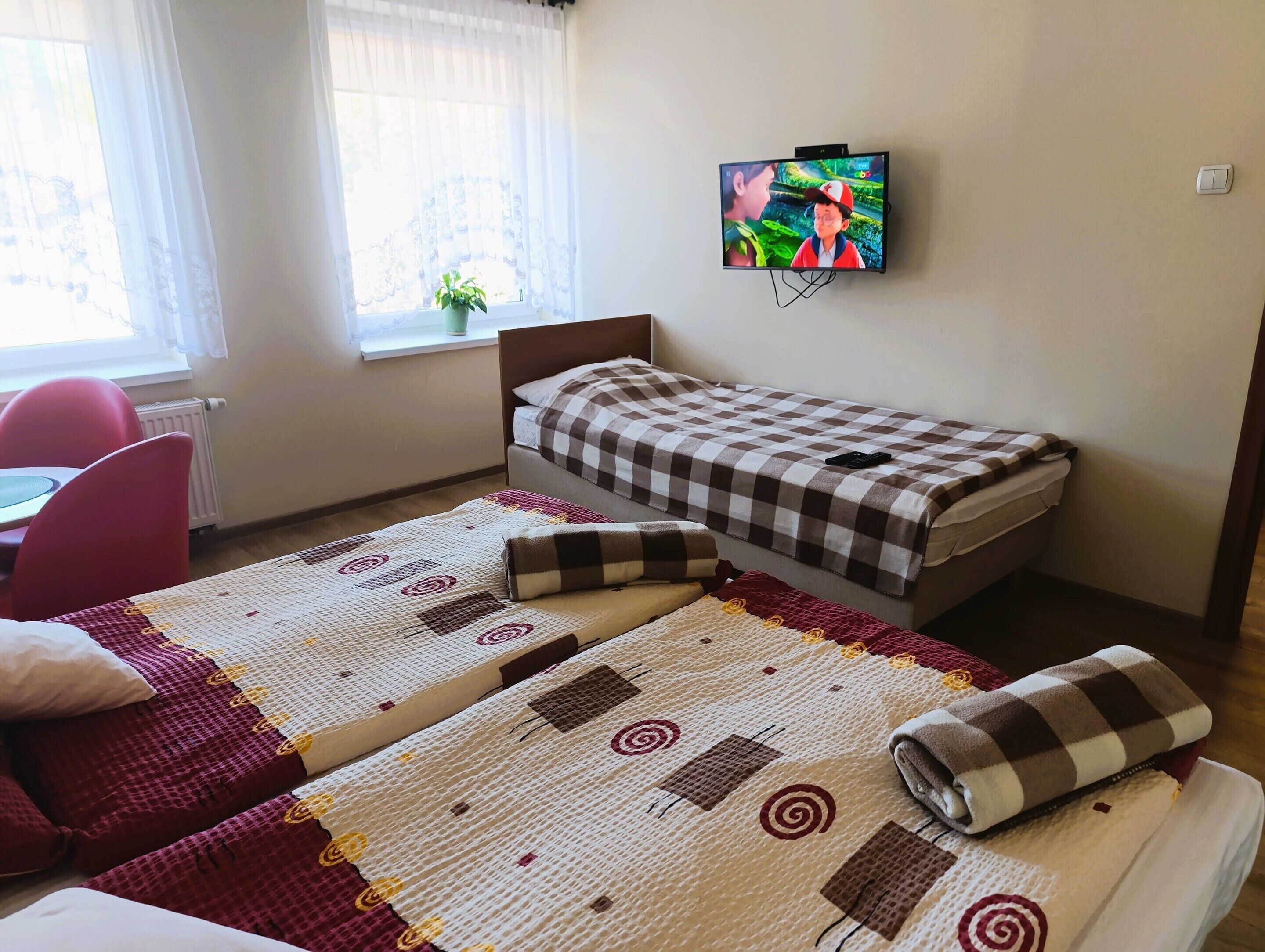 A room with two beds, a TV, a window with curtains, and a chair.