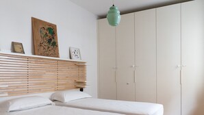 Quarto com duas camas, cabeceira de ripas de madeira, luminária pendente verde e um guarda-roupa grande.