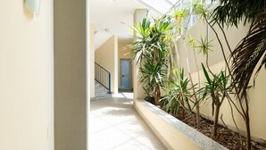 Um corredor com escadas, plantas e uma porta ao fundo.