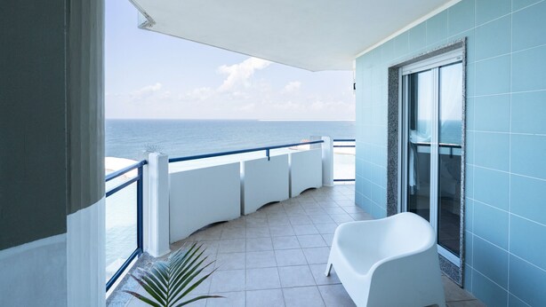 Varanda com vista para o mar, uma cadeira branca e uma porta de vidro.