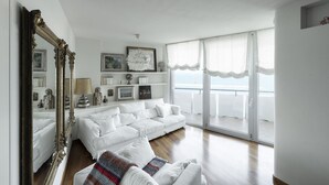 Uma sala de estar ampla com um sofá branco, um espelho grande e uma varanda com vista.