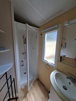Et badeværelse med brusebad, vask, vindue og spejl.