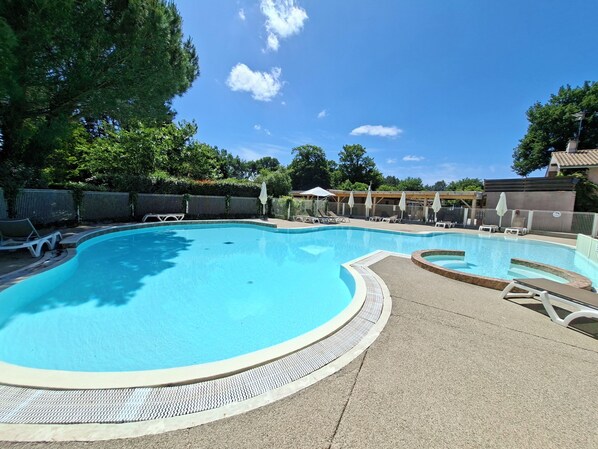 A swimming pool with lounge chairs and umbrellas, surrounded by a fence and trees. - Mobile home rental 4 pers Carcans (Carcans)