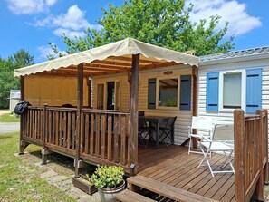 En overdækket terrasse med trægelænder, et bord med stole og en potteplante.