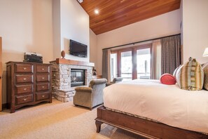 Ein Schlafzimmer mit Kamin aus Stein, einem großen Bett mit vielen Kissen, einer Holzkommode und einem an der Wand befestigten Fernseher.