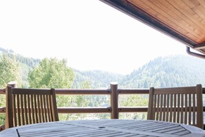 Een houten terras met een tafel en stoelen, met uitzicht op een bebost dal.
