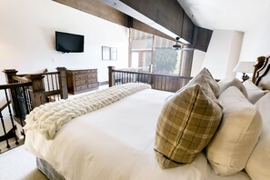Un dormitorio con una cama grande, cabecera de madera, televisor montado en la pared y balcón con vistas al exterior.