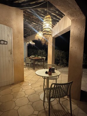 An outdoor patio with a round table and chairs, a hanging light fixture, and a door with a clock.