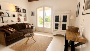 A living room with a brown sofa, a coffee table, a woven rug, a cabinet with black doors, and a vase on a wooden stand. - Welcome to Villa Sulvia, located between the sea and the hinterland of Provence. (Roquefort-les-Pins)