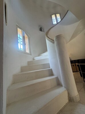 A staircase with white steps and columns, leading to a landing with a view of the outside.