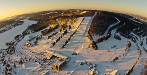 Una vista aerea di un paesaggio innevato con un grande complesso di edifici, diverse strutture più piccole e un cielo sereno.