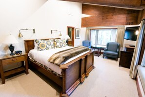 Un dormitorio con una cama grande, mesitas de noche, un televisor y una zona de estar con una silla y sofá.